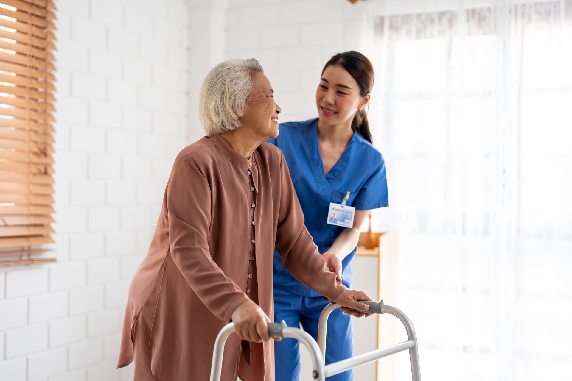 Asian senior older woman patient doing physical therapy with caregiver. Attractive specialist carer women help and support elder mature female practice walking slowly with walker at nursing home care.